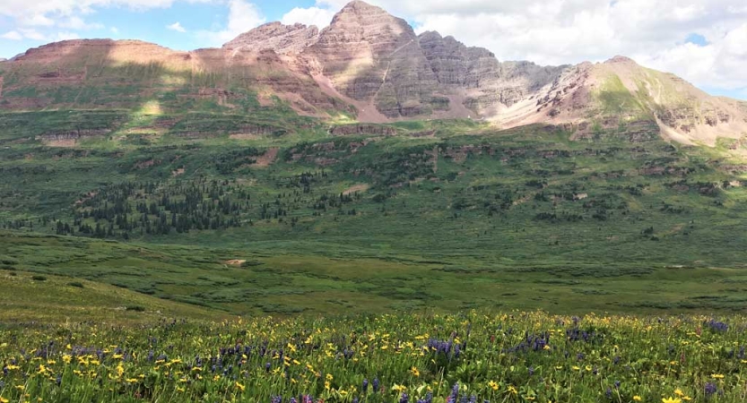 A green valley lies below a rocky mountain 